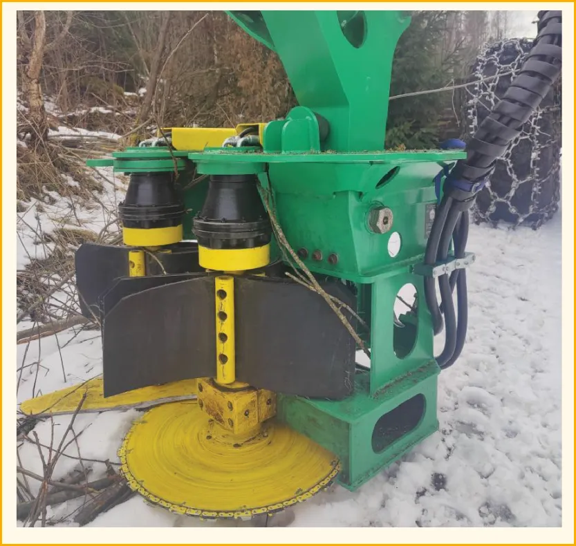 StemMaster continuously-collecting felling head in winter operation — yellow disc blade + green frame + tire chains visible in the background